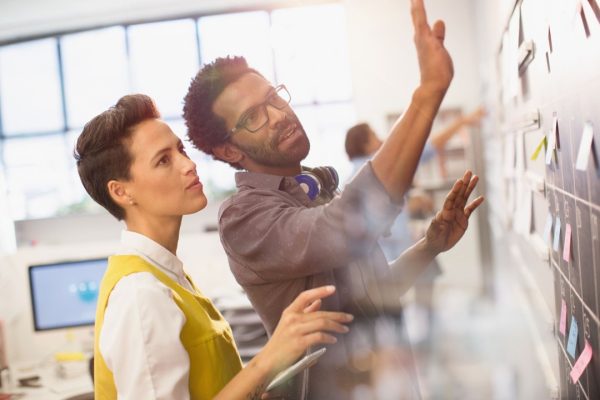 Two colleagues stand in front of a blackboard looking at sticky notes and data
